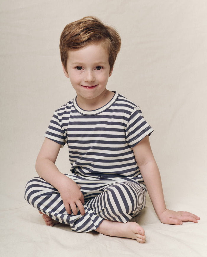 A child in The Little Boxy Crew by THE GREAT. SP25 POLO LOUNGE LITTLE, featuring a Vintage Blue Stripe design, sits comfortably on the floor against a neutral background.