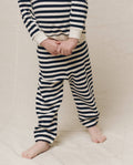 A child in the navy sailor stripe Little Stadium Sweatpant by THE GREAT. stands barefoot on the beige floor, hands clasped in front.