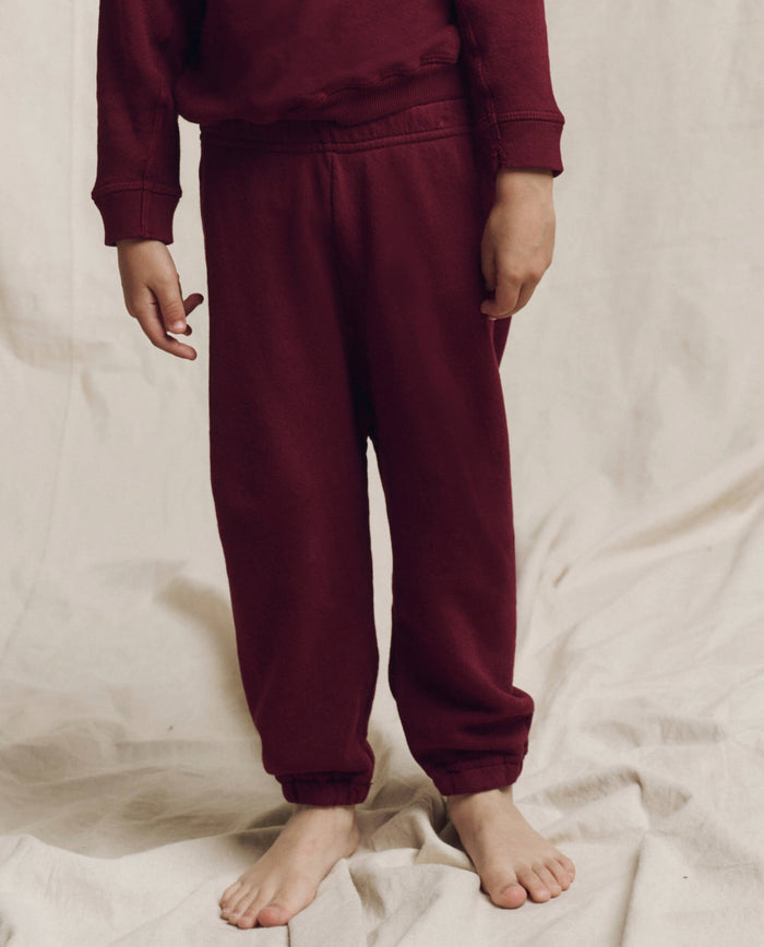 A child stands barefoot on a fabric backdrop, wearing a plum tracksuit that embodies the comfort sportswear feel of The Little Stadium Sweatpant from THE GREAT. HOL 24 LITTLE.
