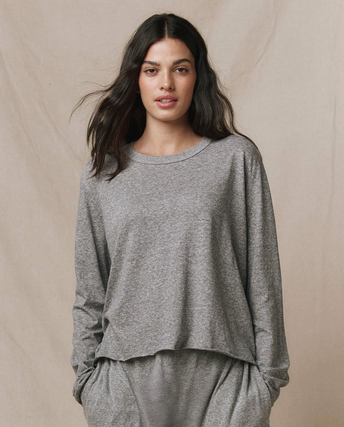 A woman wearing THE GREAT. CORE KNITS The Long Sleeve Crop Tee in heather grey with a raw hem.
