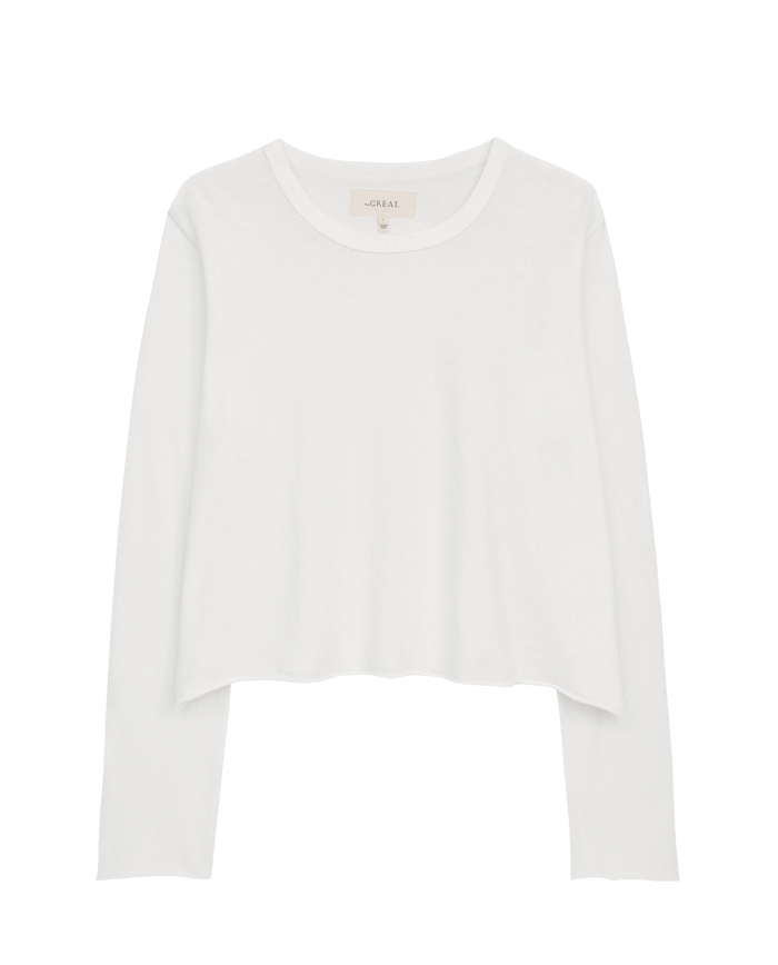 The Long Sleeve Crop Tee by THE GREAT. CORE KNITS in True White showcases long sleeves, a round neckline, and a raw hem against a plain black background.