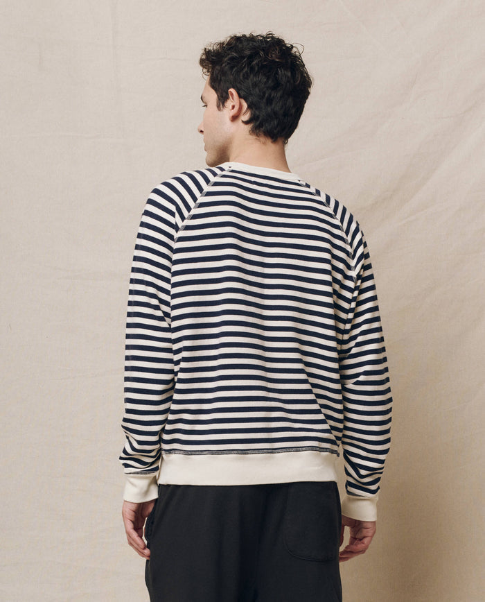 Person wearing The Men's College Sweatshirt in Navy Sailor Stripe, by THE GREAT. SP25 POLO LOUNGE MEN, facing away against a beige background.