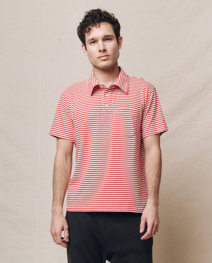 A person wearing The Men's Lacrosse Polo in Sun Cherry Stripe by THE GREAT. SP25 POLO LOUNGE MEN stands before a beige backdrop.