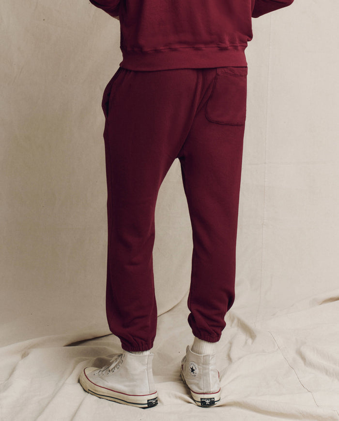A person wearing The Men's Stadium Sweatpant in plum from THE GREAT. HOL 24 MEN and white high-top sneakers stands effortlessly on a light fabric backdrop.