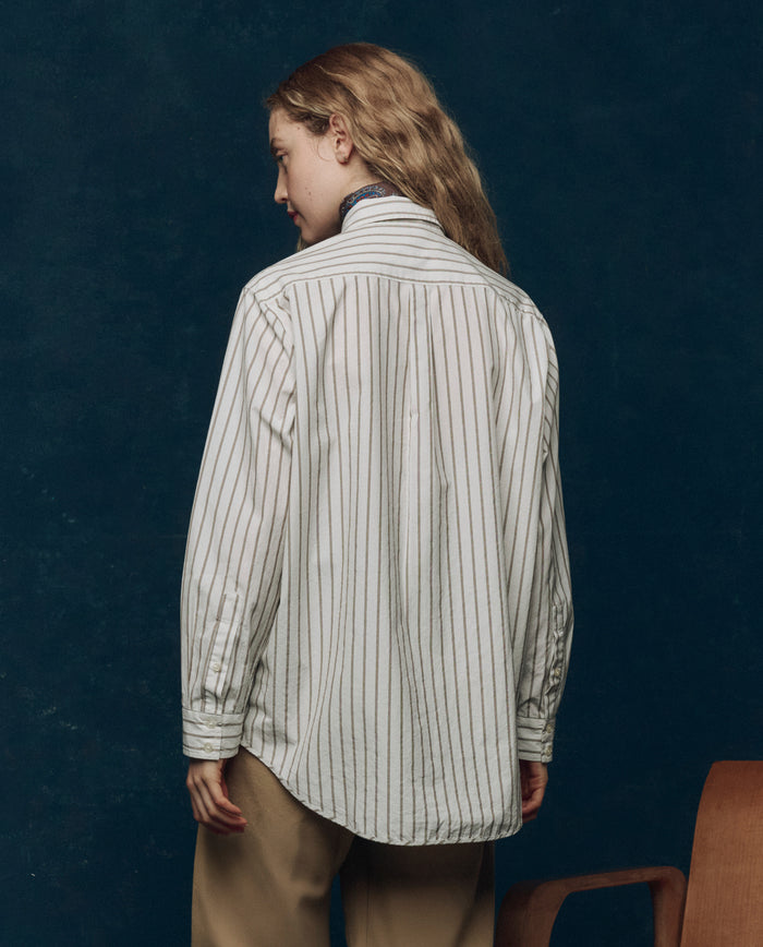 A woman wearing THE GREAT. PS26 COLLECTORS "The Menswear Button Up" in Ivy League Stripe—a vintage-inspired work shirt with classic stripes.