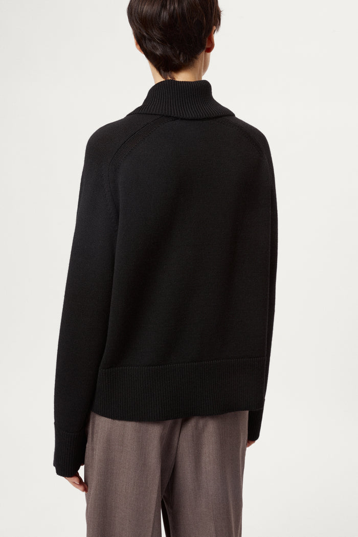 Person wearing a black sweater and gray pants on a white background