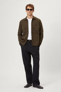Man wearing a merino green jacket, white t-shirt, black pants, and sunglasses on a white background