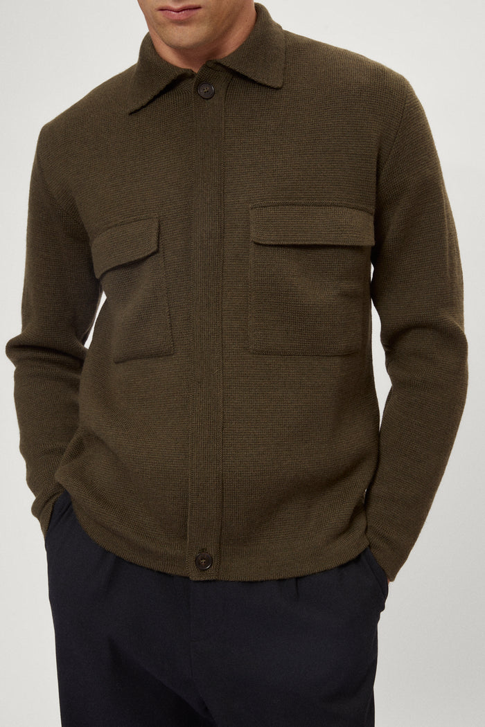 Man wearing a merino green jacket, white t-shirt and blue pants on a white background