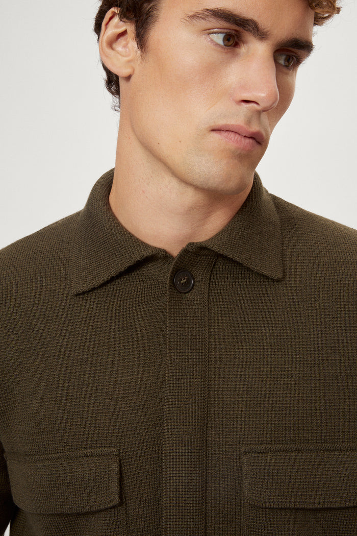 Man wearing a merino green jacket, white t-shirt and blue pants on a white background