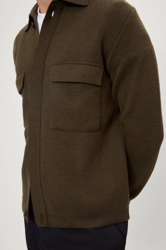 Man wearing a merino green jacket, white t-shirt and blue pants on a white background