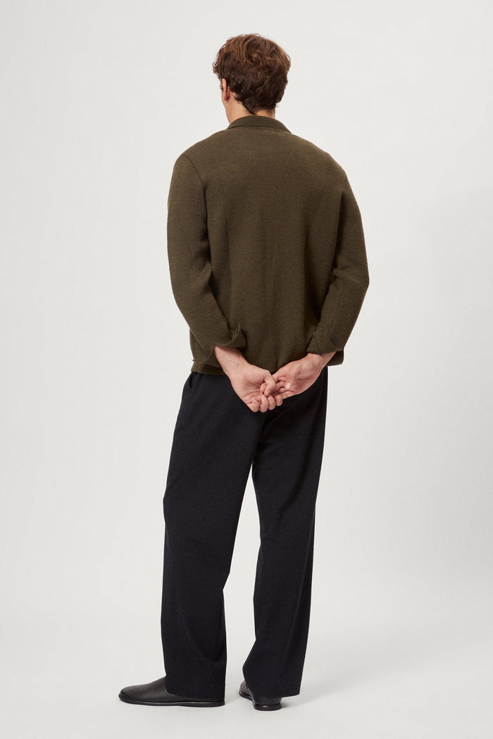 Man wearing a merino green jacket, white t-shirt and blue pants on a white background