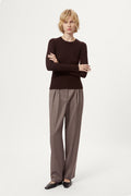 Woman wearing a dark brown sweater and light brown pleated pants on a white background