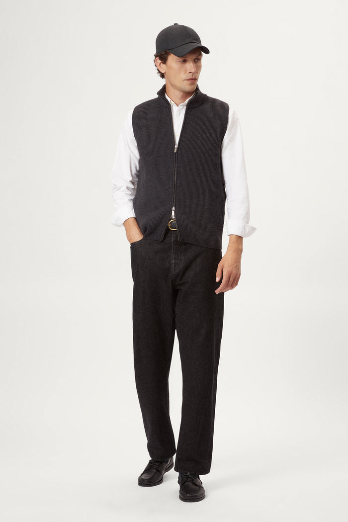 Man wearing a dark gray zip-up vest over a white shirt on a white background
