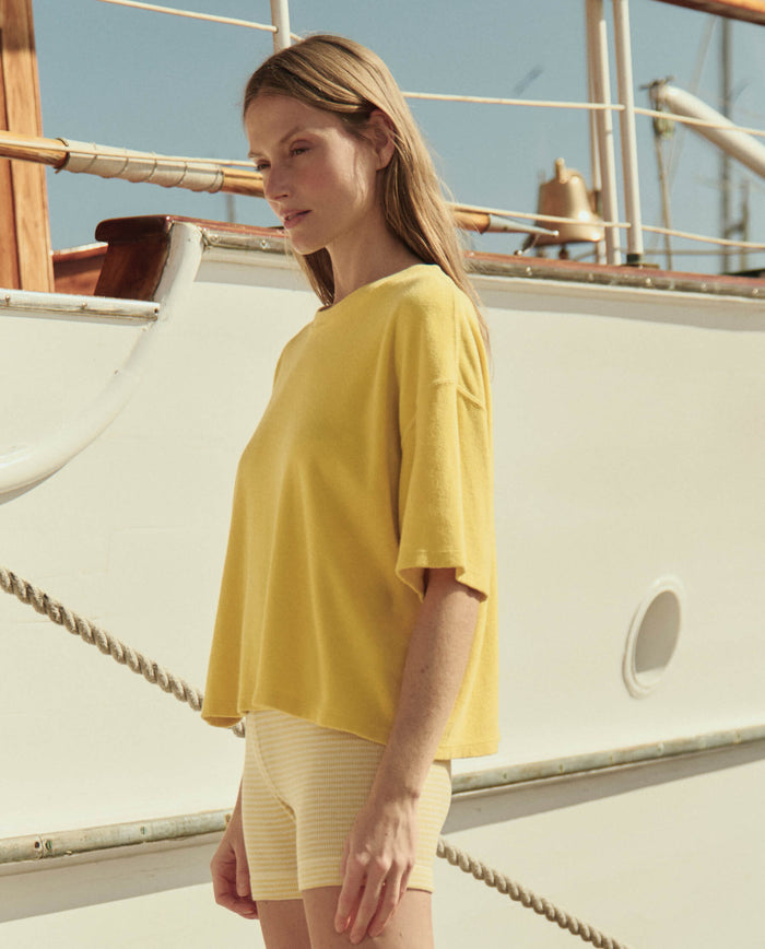 A woman stands on a boat deck in THE GREAT. SU26's The Micro Terry Track Crew -- Margarita, with sunlight illuminating the scene.
