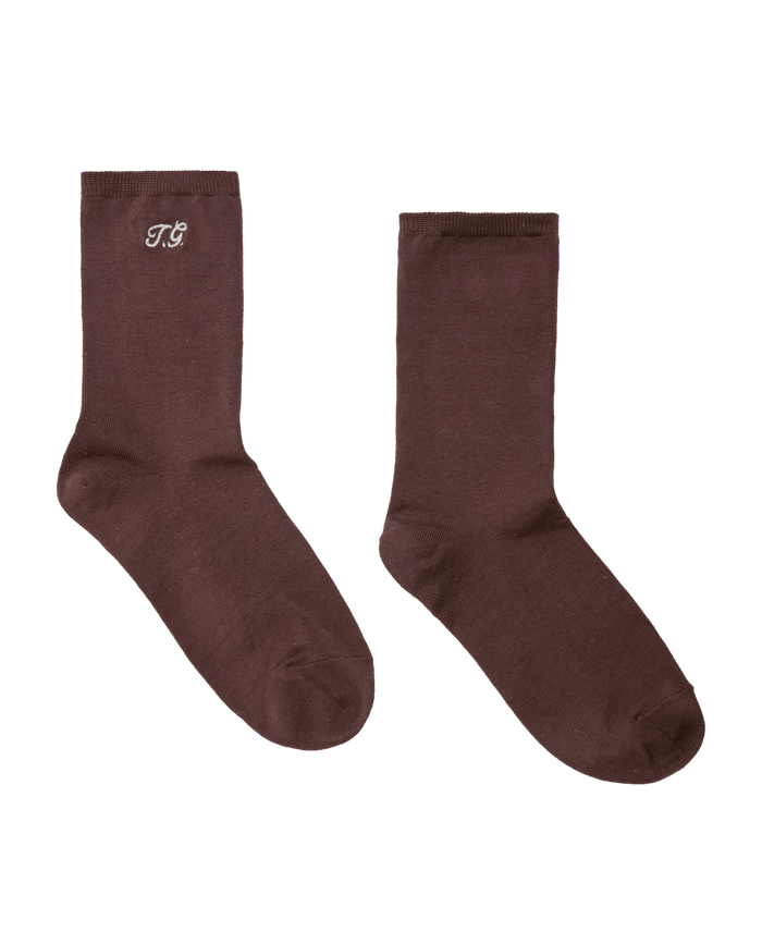 A pair of The Monogrammed Trouser Sock in Chocolate by THE GREAT., laid flat, featuring "TG" monogrammed in white on the ankle of the left sock.