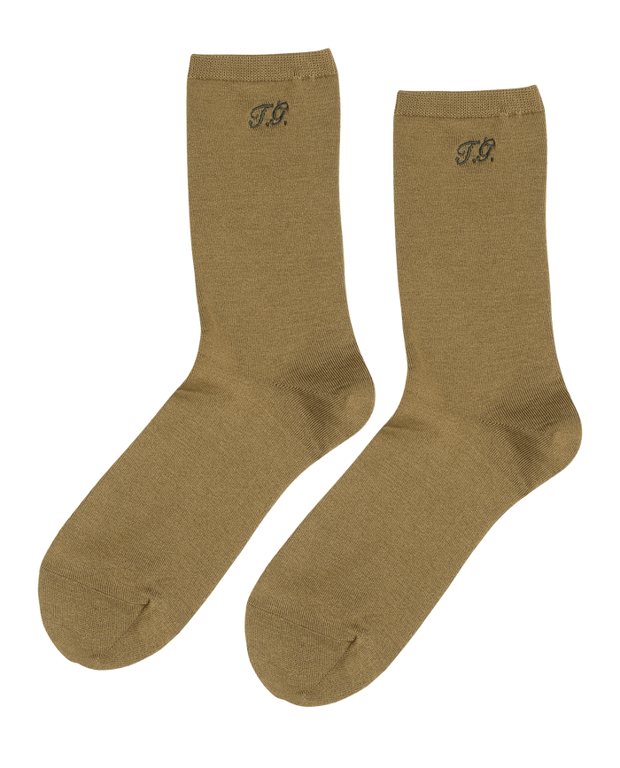 A pair of THE GREAT. Monogrammed Trouser Socks in golden ochre with "T.G." initials near the top.