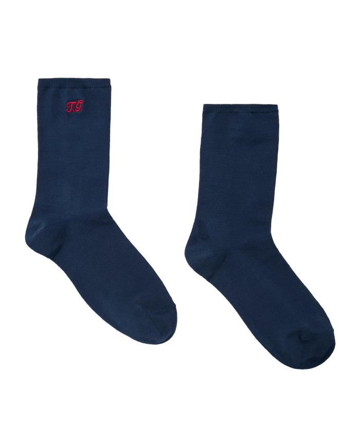 A pair of THE GREAT. F26 D1 The Monogrammed Trouser Socks in navy, laid flat on a white background, featuring a small red “TS” monogram on the upper side of one sock.