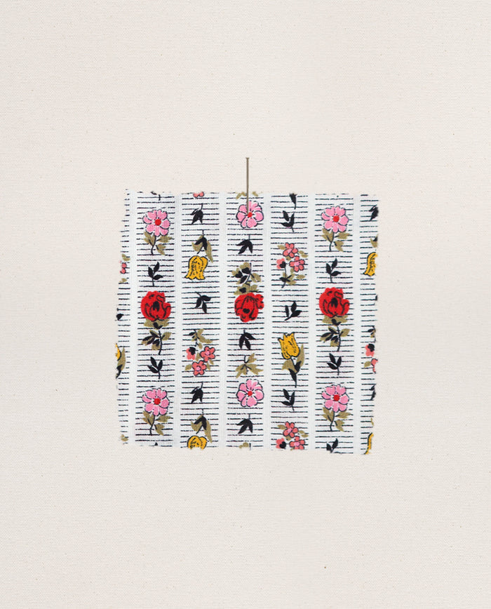 A swatch of THE GREAT. PS26 SLEEP’s The Ruffle Tank Night Dress in Ribbon Floral—showing red, pink, and yellow flowers on white—is centered on an off-white surface.