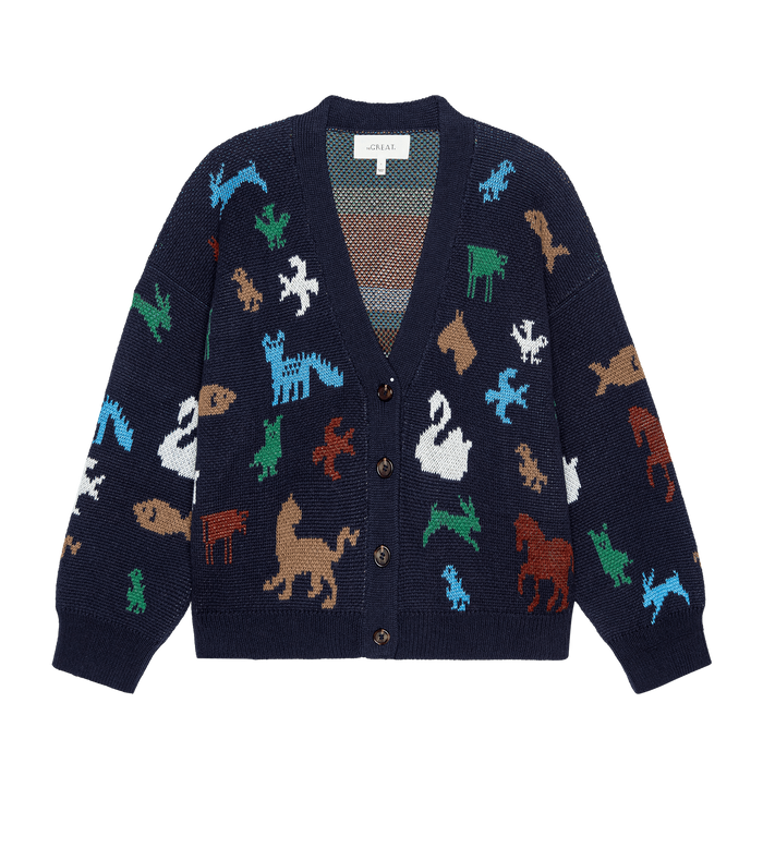 The Pictograph Slouch Cardigan by THE GREAT. PS26 in navy features multicolored animal patterns in a birdseye jacquard knit with front button closure, shown on a plain white background.