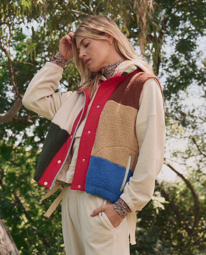 Someone wearing The Plush Color Block Sierra Vest in Canyon Multi by THE GREAT. SP26 TGO, layered over a cream outfit, stands outdoors near trees.
