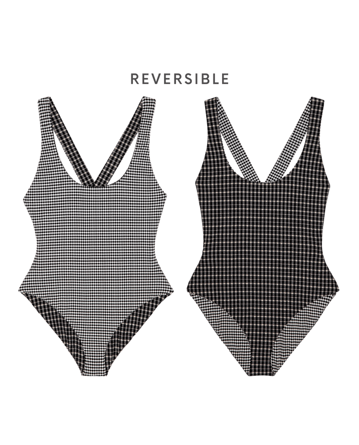 Two views of THE GREAT. SP26 SWIM's The Reversible Cross-Back One Piece in Black & Cream Check are shown, with a scoop neckline and black-and-white checks in varying sizes on each side.