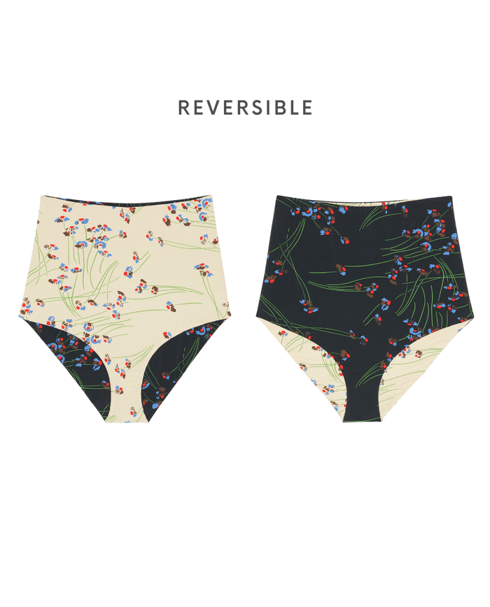 The Reversible High Rise Covered Brief by THE GREAT. SP26 SWIM is shown in Windblown Bouquet, featuring vintage-inspired floral patterns on cream and black backgrounds. Text above reads "REVERSIBLE," perfect for fans of retro 50s swimwear style.