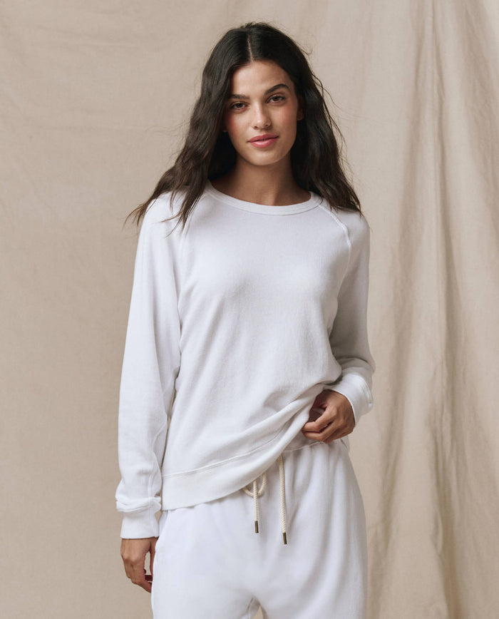 A woman wearing the SP26 New Knits "The Rookie Sweatshirt. Solid -- True White" with matching sweatpants stands in front of a beige fabric backdrop.