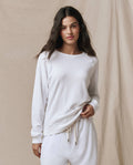 A woman wearing the SP26 New Knits "The Rookie Sweatshirt. Solid -- True White" with matching sweatpants stands in front of a beige fabric backdrop.