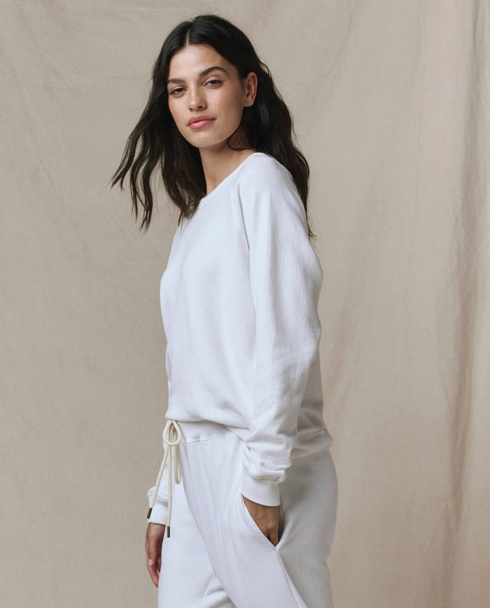 A person stands against a neutral backdrop wearing SP26 New Knits’ The Rookie Sweatshirt in Solid -- True White, paired with matching sweatpants, with one hand in their pocket.