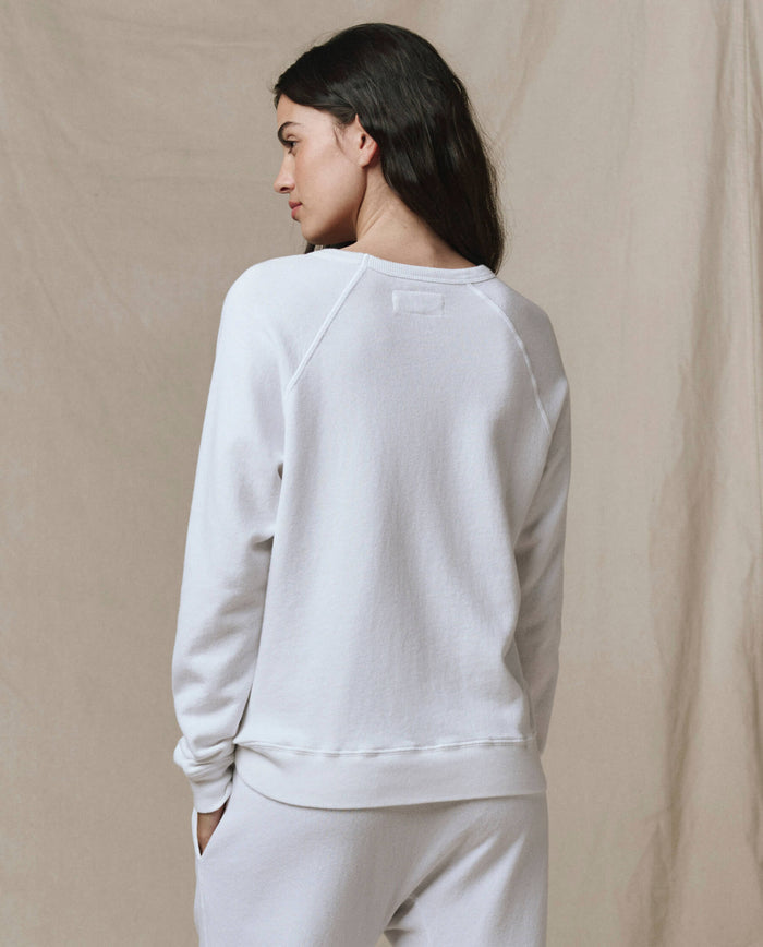 A woman with long dark hair stands with her back to the camera, wearing the SP26 New Knits "The Rookie Sweatshirt. Solid -- True White" and matching pants against a neutral background.