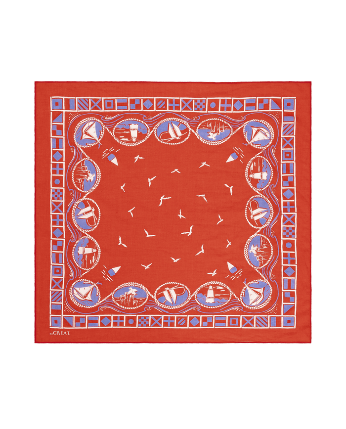 The Sailboat Bandana by THE GREAT. SU26 is a red vintage scarf featuring a blue and white nautical border with ships, knots, flags, and seagulls in the center.
