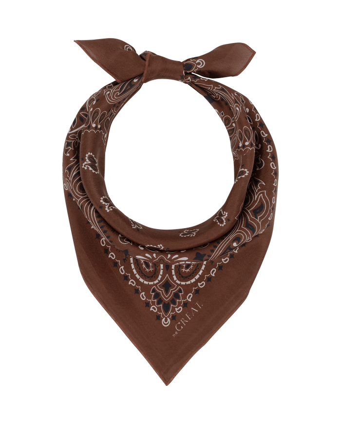 The Silk Bandana in Chocolate by THE GREAT. F26 COLLECTORS features a vintage-inspired brown hue with a classic white paisley pattern, crafted from lightweight silk and styled in a loose knot, showcased on a plain white background.