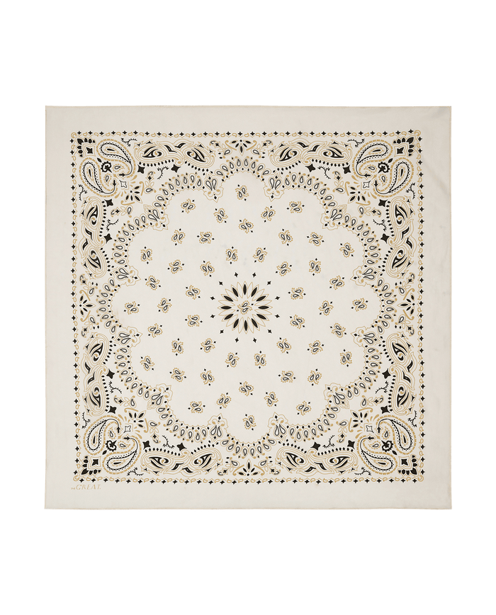 The Silk Bandana – Cream by THE GREAT. F25 COLLECTORS is a square white silk bandana with black and gold paisley and floral patterns, a central scalloped design, and decorative border for a refined, timeless vintage look.