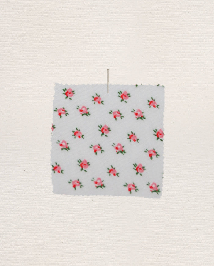 A square swatch of The Jersey Sleep Robe — Calico Rose by THE GREAT. PS26 SLEEP, featuring a white fabric with small pink rose prints, is pinned to a light background.