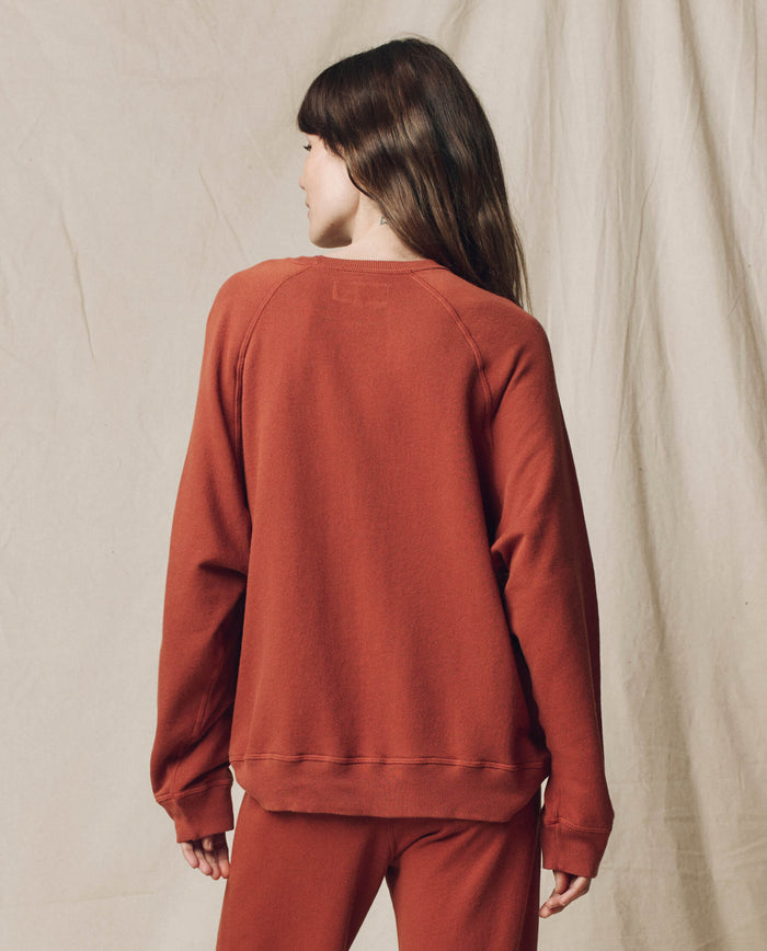 Person with long brown hair wears THE GREAT.'s The Slouch Sweatshirt, Solid -- Brick, from F25 SEASONAL KNITS, with matching pants. Stands back to camera against a neutral backdrop for a cozy, vintage-inspired Los Angeles look.