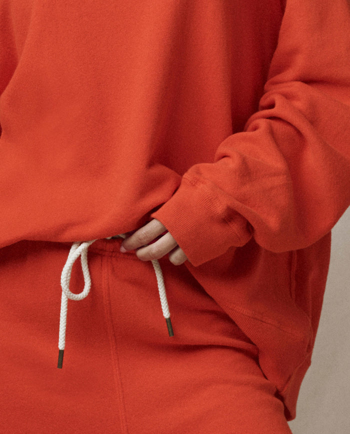 A person wearing THE GREAT.’s The Slouch Sweatshirt in Persimmon, with one hand in their pocket—an effortlessly cool look from the SP26 SEASONAL CORE, handcrafted in Los Angeles.