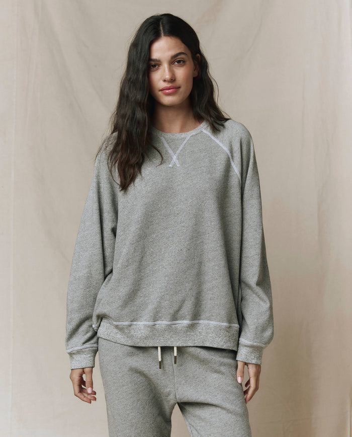 A person wears THE GREAT. CORE KNITS The Slouch Sweatshirt in Varsity Grey with matching straight-leg sweatpants, both featuring fuller sleeves, standing before a neutral background.