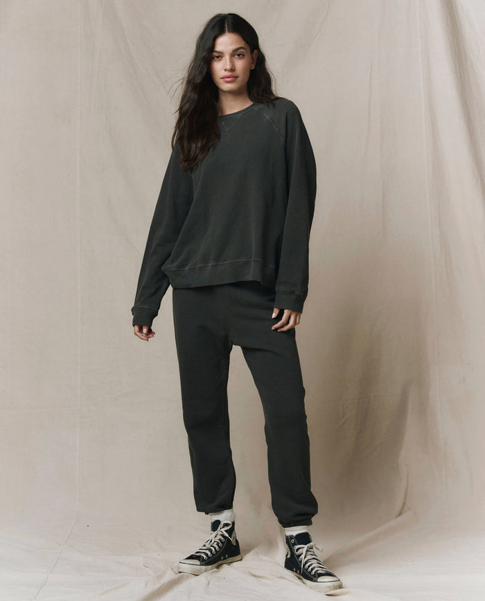 A woman wears THE GREAT. CORE KNITS The Slouch Sweatshirt in solid washed black paired with black pants.