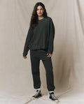A woman wears THE GREAT. CORE KNITS The Slouch Sweatshirt in solid washed black paired with black pants.