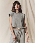 A woman stands against a plain fabric backdrop, featuring "The Square Tee" in heather grey by THE GREAT. SU23 CORE KNITS, paired with matching sweatpants.