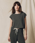 A woman with long brown hair stands against a plain backdrop, wearing The Square Tee in Washed Black by THE GREAT. SU23 CORE KNITS and matching drawstring pants.