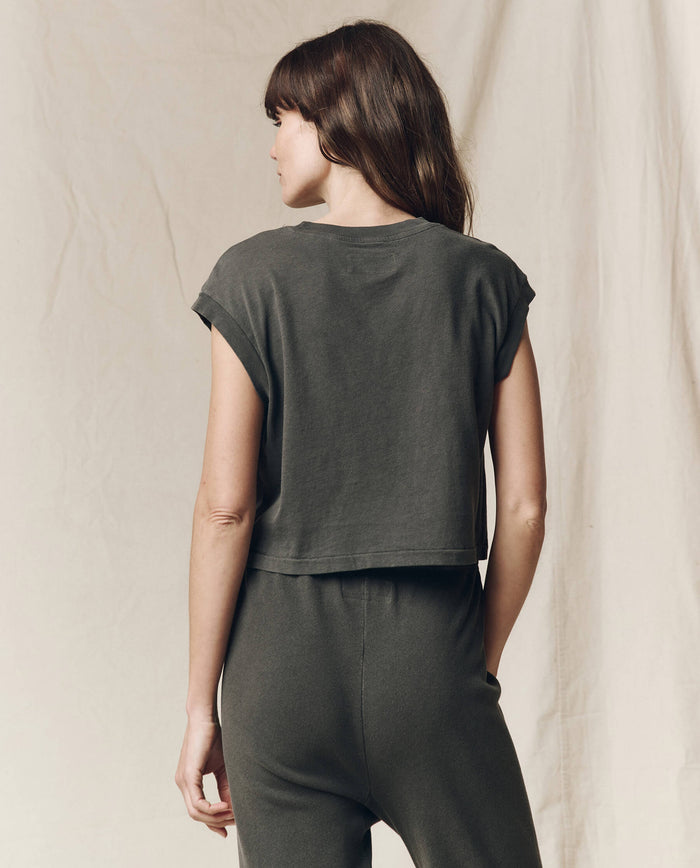 A person with long hair faces away, wearing The Square Tee in Washed Black by THE GREAT. SU23 CORE KNITS, paired with matching pants, against a neutral background that complements the outfit's simplicity.