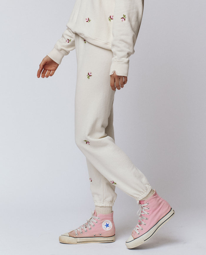 Wearing THE GREAT.’s The Stadium Sweatpant, Embroidered in Washed White with Embroidered Roses by H25 ROSEBUD, paired with light pink high-top Converse sneakers for a vintage athletic-chic look.