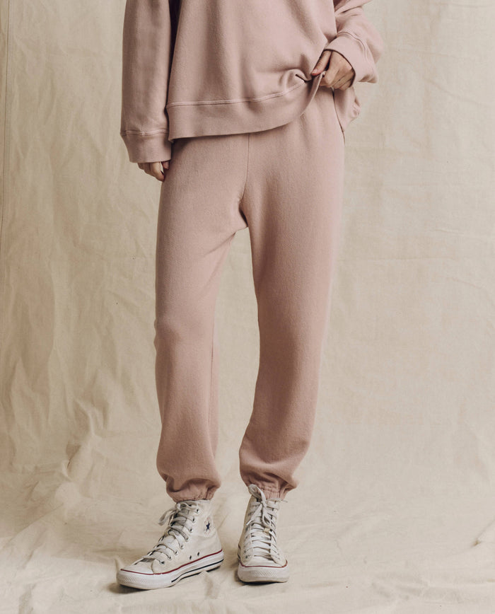 Dressed in THE GREAT. F26 SEASONAL CORE’s The Stadium Sweatpant. Solid in Ballet Pink, paired with a relaxed matching sweatshirt and crisp white high-top sneakers, this look exudes effortless Los Angeles style against a beige fabric backdrop.