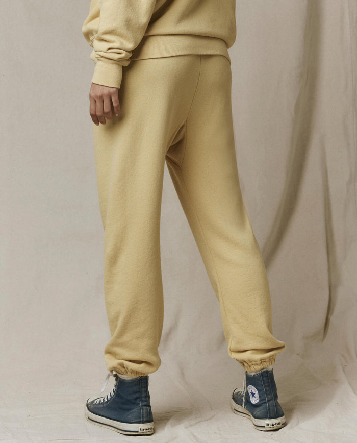 A person wears THE GREAT. SP26 SEASONAL CORE The Stadium Sweatpant in Butter Yellow, paired with a matching sweatshirt and blue high-top sneakers, standing against a neutral backdrop with vintage athletic wear vibes.