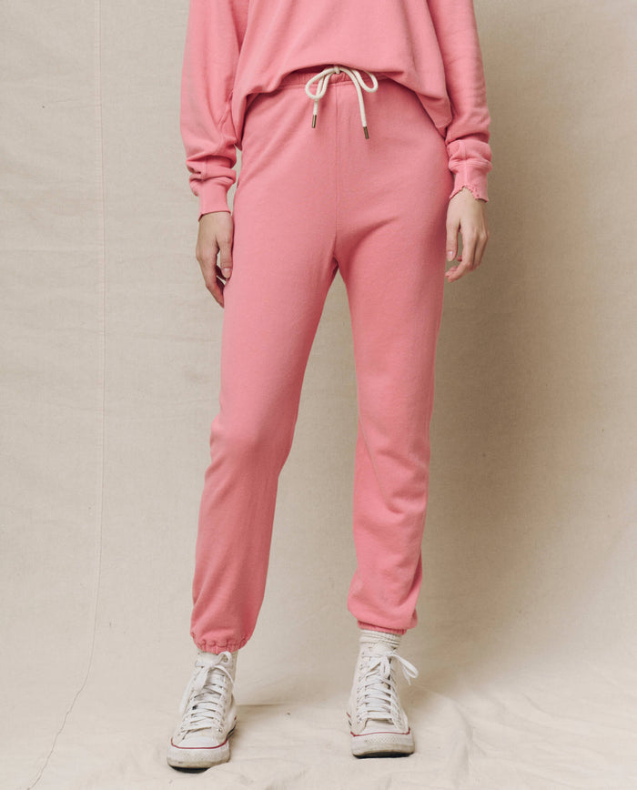 Dressed in The Stadium Sweatpant. Solid -- Confetti by THE GREAT. SP25 KNITS and a pink sweatshirt, paired with white high-top sneakers, a person stands against a beige background.