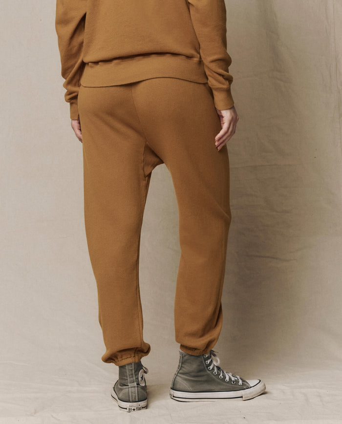 Person wearing THE GREAT. SU26 SEASONAL CORE The Stadium Sweatpant, Solid -- Cork, paired with a matching sweatshirt and gray high-top sneakers, photographed from behind on a neutral fabric background.