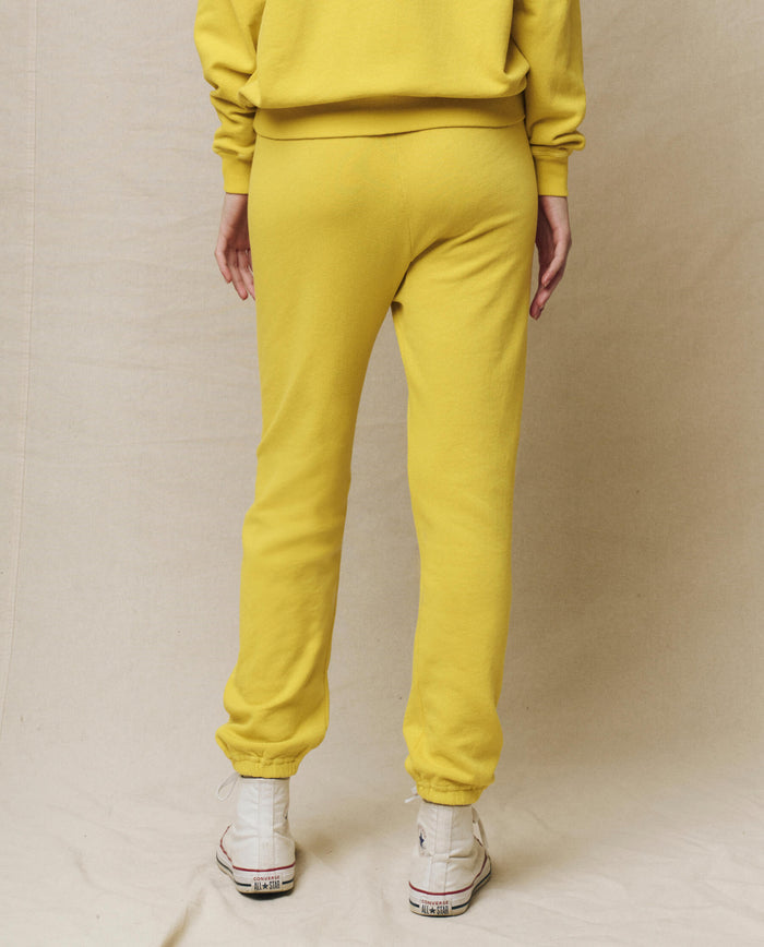 A person stands with their back to us, showcasing the athleisure style in The Stadium Sweatpant Solid -- Daffodil from THE GREAT. SP25 KNITS, paired with white sneakers against a neutral background.