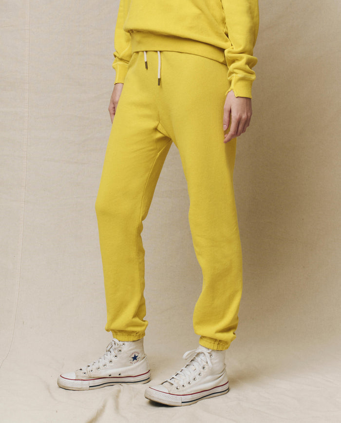 A model in The Stadium Sweatpant - Daffodil by THE GREAT. SP25 KNITS pairs it perfectly with white high-top sneakers, standing against a plain backdrop, embodying comfort and style.