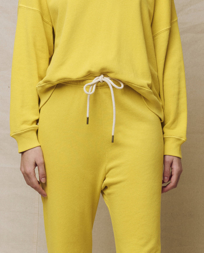 A person is modeling a yellow sweatshirt with THE GREAT. SP25 KNITS, The Stadium Sweatpant in Daffodil, epitomizing athleisure style against a neutral backdrop.
